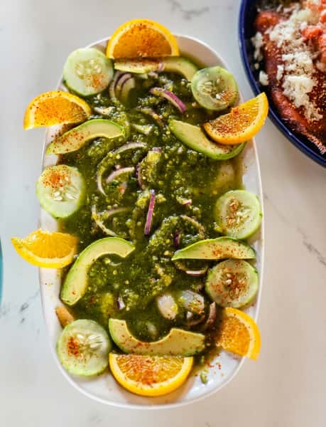 Aguachile with shrimp, green sauce, red onion, avocado, cucumber, and orange slices.