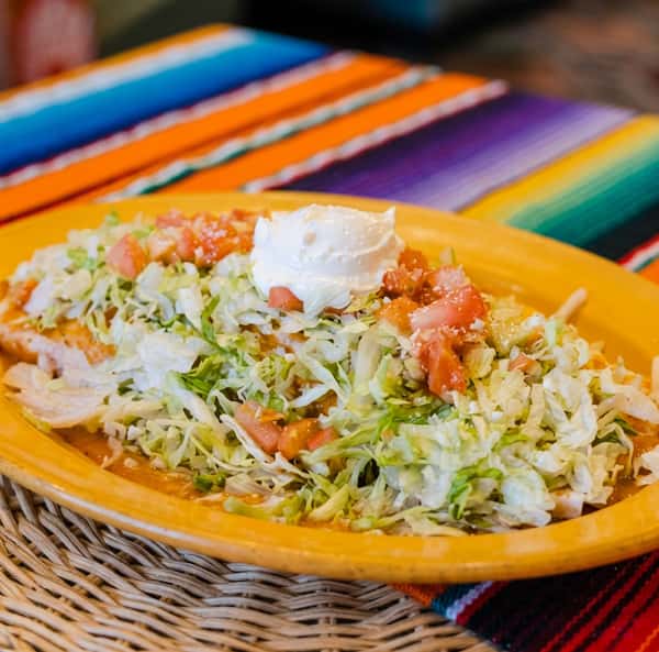 Enchiladas covered with shredded lettuce, diced tomatoes, and a dollop of sour cream on a yellow plate.