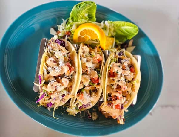 Three fish tacos on a blue plate, garnished with lettuce and an orange slice.