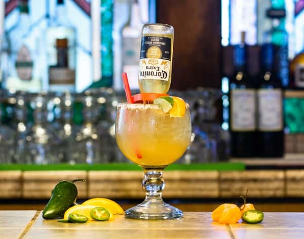 Margarita with an inverted Corona beer, lime, and orange slices, garnished with salt, peppers, and red straw.