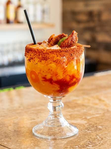 Margarita in a wide glass, rimmed with red spice, garnished with fruit and lime slice.
