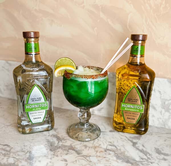 Green frozen margarita with chili-lime rim, lemon/lime slices, and two Hornitos tequila bottles.