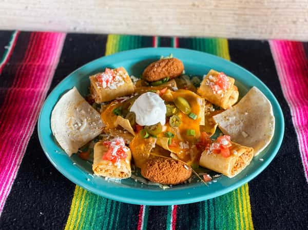 Nachos with melted cheese, jalapeños, sour cream, green onions, and mini taquitos on a blue plate.