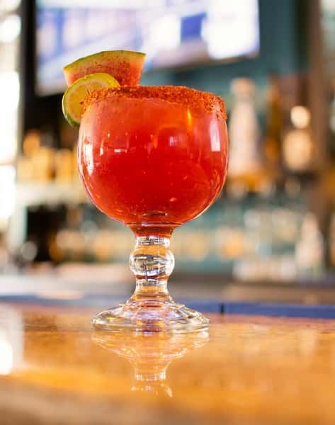 Orange cocktail in a goblet glass with a chili-salt rim, garnished with a lime slice and watermelon wedge.