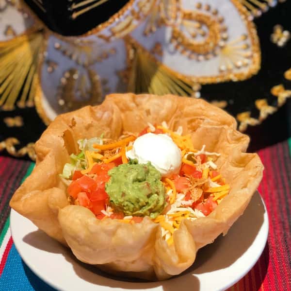 Taco salad in a fried tortilla bowl with guacamole, sour cream, diced tomatoes, lettuce, and shredded cheese.
