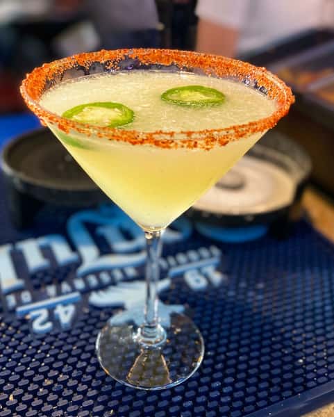 Margarita with sliced jalapeños and a chili salt rim, on a blue bar mat.