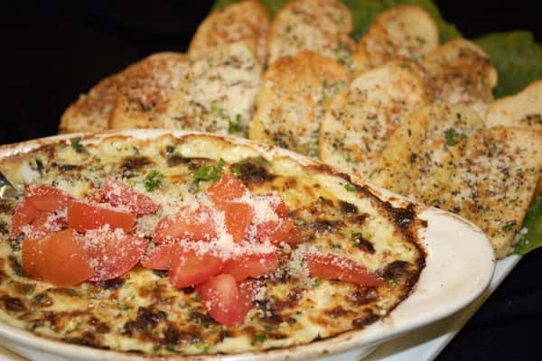 spinach and artichoke dip topped with tomatoes and a side of sliced garlic bread