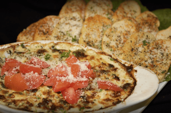 spinach and artichoke dip topped with tomatoes and a side of toasted bread