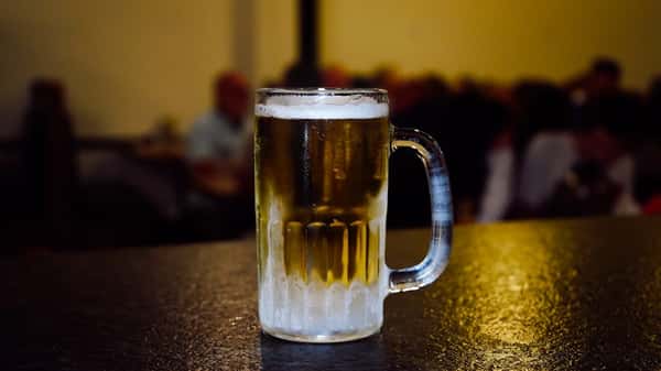 Chilled frosted glass mug filled with golden draft beer, sitting on a dark bar counter with a softly lit background, capturing a refreshing and inviting pub ambiance.