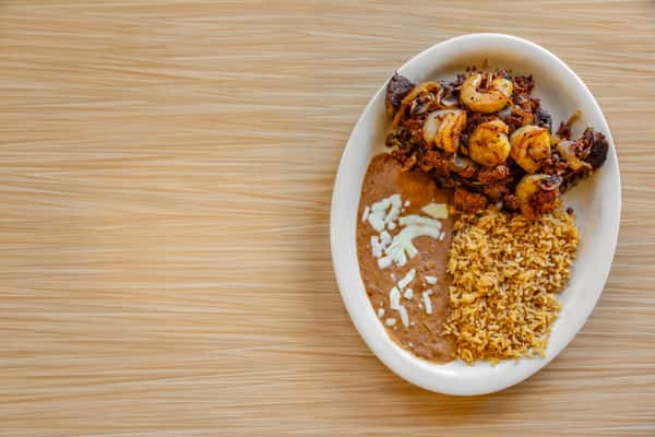 Grilled steak topped with sautéed shrimp, onions, and crumbled chorizo, served with refried beans and seasoned Mexican rice on an oval plate.