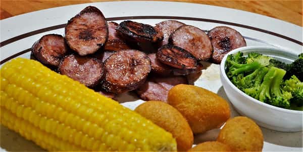 sliced pork with a side of corn and hushpuppues