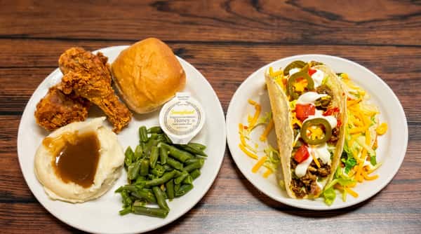 Two plates of food: fried chicken, mashed potatoes, green beans, roll; and a taco with beef, cheese, lettuce, and jalapeños. A "Don's Family Style Buffet" sign is above.