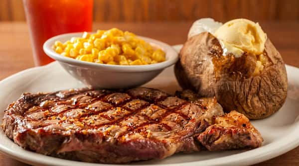 Grilled steak with grill marks, a baked potato topped with butter and sour cream, and a side of corn.