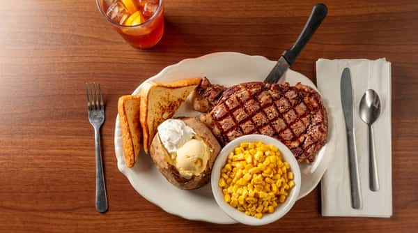Grilled steak with grill marks, baked potato with sour cream and butter, corn, and toast slices on a white plate.