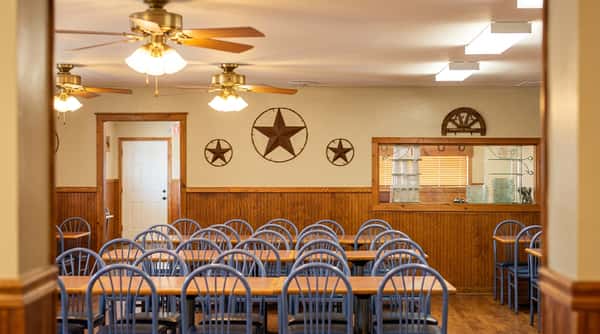 Restaurant dining room with rows of tables and chairs, wood paneling, ceiling fans, and metal star decorations.