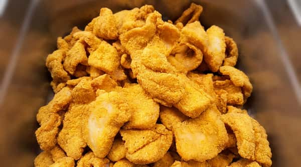 Golden-fried fish fillets or nuggets, coated in a seasoned, golden-yellow breading, piled together.