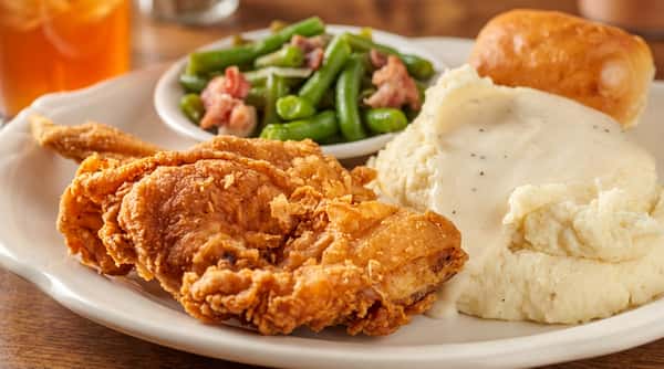 Fried chicken with mashed potatoes, gravy, and green beans with ham on a white plate.