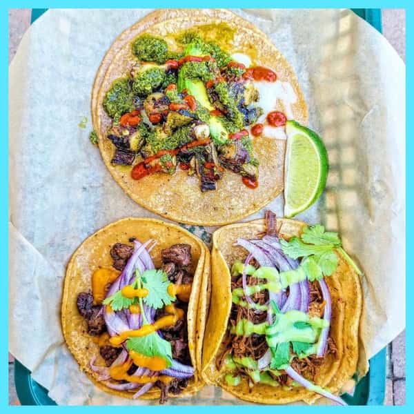 Three colorful Milagro Tacos Cantina tacos featuring vibrant roasted vegetables, diverse meats, fresh lime, and flavorful sauces.