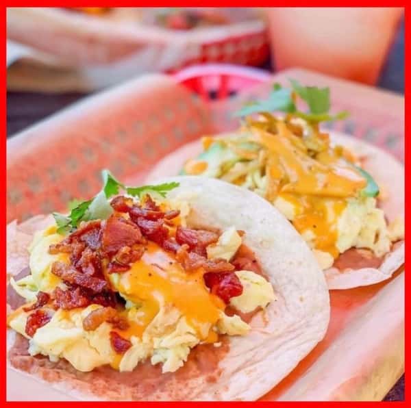 Two Milagro Tacos Cantina breakfast tacos topped with scrambled eggs, crispy bacon, and orange sauce.