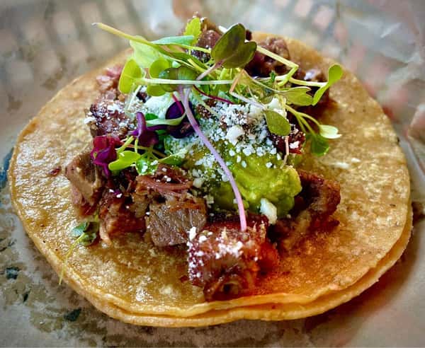 Milagro Tacos Cantina's savory beef taco with vibrant guacamole, cotija cheese, and fresh microgreens on a golden corn tortilla.