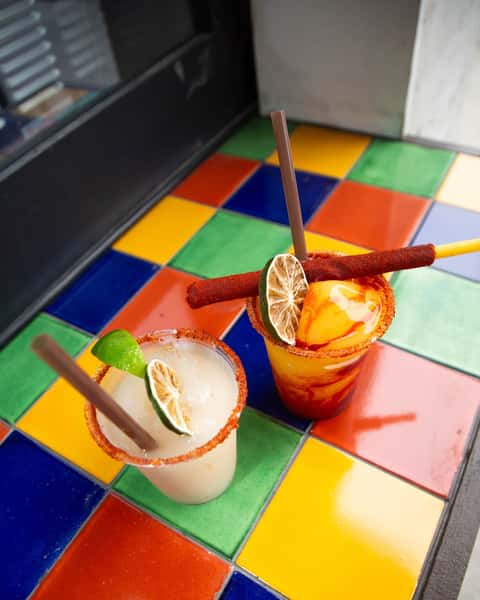 Milagro Tacos Cantina's vibrant blended drinks with lime and chili rims on a colorful tiled table.