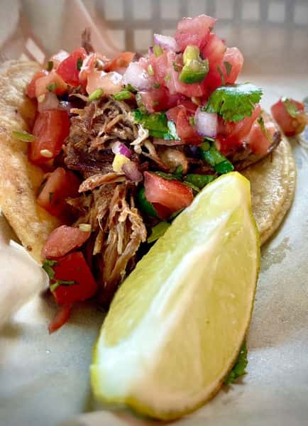 A vibrant shredded meat taco topped with colorful pico de gallo and a fresh lime wedge from Milagro Tacos Cantina.
