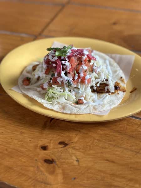 Milagro Tacos Cantina's vibrant taco with shredded cabbage, red pico, white crema, and pickled red onions on a yellow plate.