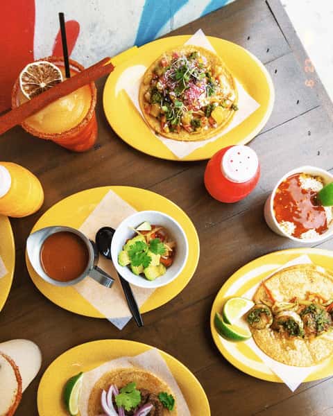 Milagro Tacos Cantina's vibrant spread of colorful tacos on bright yellow plates, a spicy frozen drink, and fresh guacamole on a wooden table.