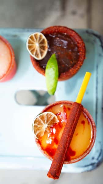 Vibrant spicy cocktails with chili-rimmed glasses, lime, and a tamarindo candy stick, served at Milagro Tacos Cantina.
