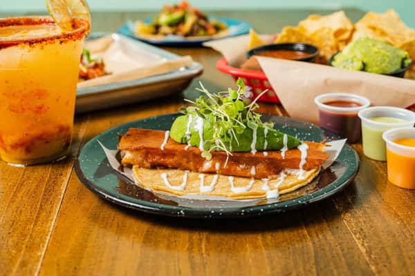 A vibrant spread of Milagro Tacos Cantina's Mexican food featuring a large taco, margarita, guacamole, and chips on a wooden table.