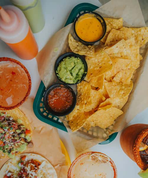 Vibrant Milagro Tacos Cantina feast featuring golden tortilla chips, guacamole, salsa, queso, fresh tacos, and colorful drinks.
