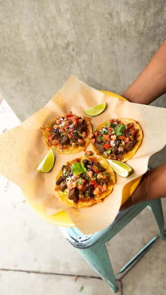 Vibrant Milagro Tacos Cantina street tacos with meat, pico de gallo, and lime wedges served on a yellow plate.