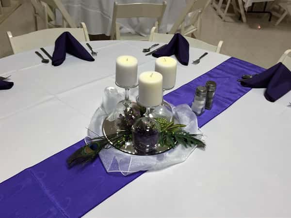 circular table with a tablecloth, folded napkins and a floral centerpiece with candles