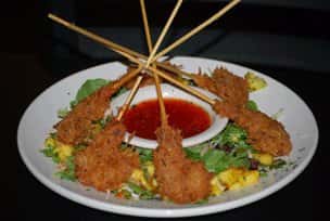 Breaded and deep fried shrimp skewers served with dipping sauce on a bed of lettucesprinkled with corn