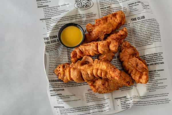 Golden-brown fried chicken tenders arranged on deli-style paper with a side of honey mustard dipping sauce — a classic appetizer or entrée option.