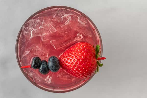 Iced berry cocktail with a vibrant pink hue, topped with a fresh strawberry and skewered blueberries — a fruity and refreshing drink ideal for summer menus.