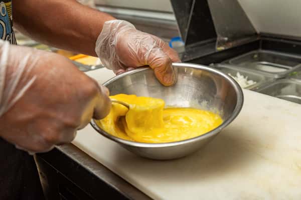 Close-up of a chef whisking eggs in a stainless steel bowl while wearing food-safe gloves — a behind-the-scenes look at fresh breakfast preparation in a professional kitchen.