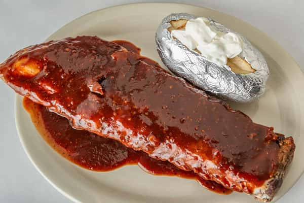Full rack of saucy barbecue ribs served with a foil-wrapped baked potato topped with sour cream — a smoky, tender Southern-style entrée perfect for hearty appetites.