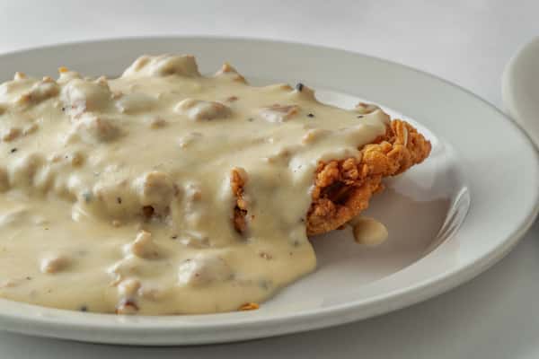 Southern-style chicken fried steak generously smothered in creamy sausage gravy, served on a white plate — a hearty and comforting Southern favorite.