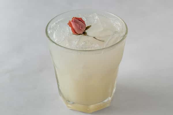 Elegant white cocktail served over ice in a short glass, garnished with a delicate dried rosebud — a floral-inspired drink perfect for upscale or romantic settings.