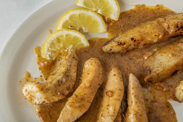 Grilled chicken tenders topped with a savory lemon pepper sauce and served with fresh lemon slices — a zesty and flavorful entrée with a light, herbed finish.