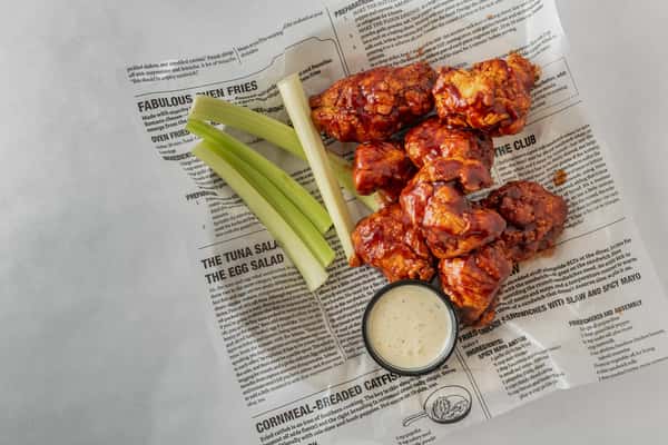 Sticky barbecue chicken wings served with crisp celery sticks and a side of ranch dressing on deli-style paper — a bold and saucy appetizer ideal for game day.
