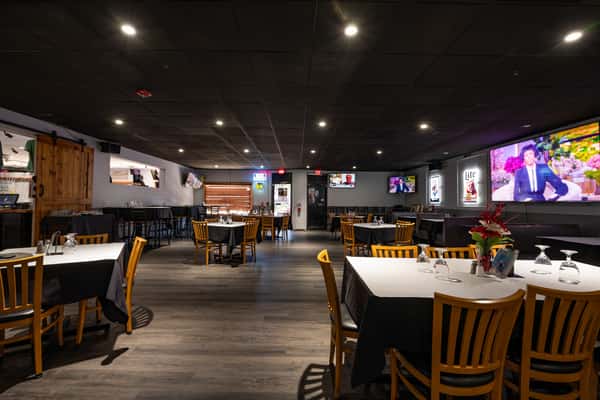Spacious dining room with black ceiling, wood flooring, and TVs along the walls, offering a cozy setting for casual dining and sports entertainment.