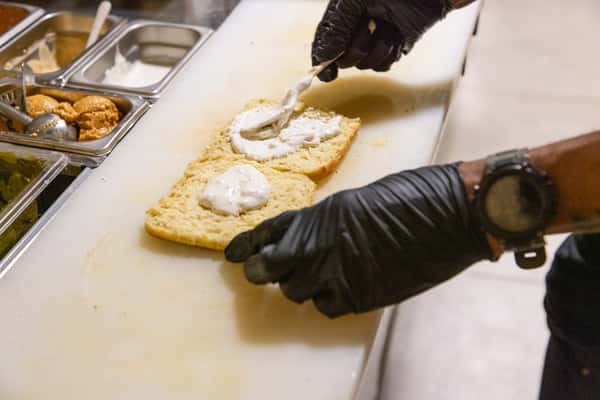 Kitchen staff preparing artisan sandwiches with fresh ingredients and house-made spreads in a professional restaurant kitchen.