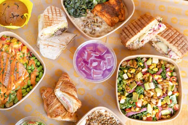 Colorful café spread featuring artisan sandwiches, fresh salads, grain bowls, pastries, and handcrafted beverages.