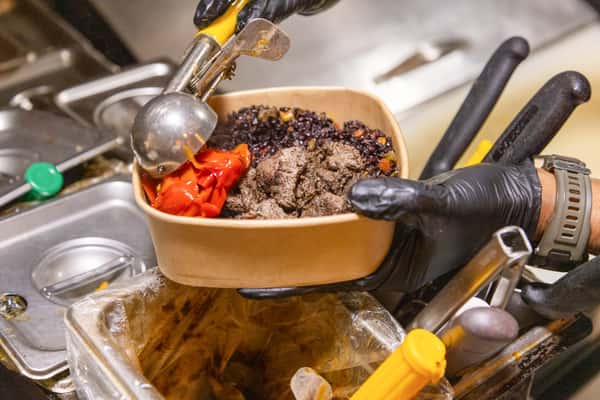 Restaurant team member preparing a fresh grain bowl with roasted vegetables and wholesome ingredients in a commercial kitchen.