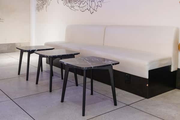 Modern restaurant lounge seating with white banquette booths, marble-top tables, and a clean contemporary dining atmosphere.
