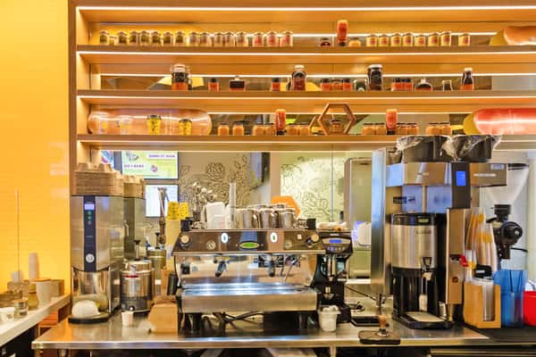 Bright modern café interior with open coffee bar, specialty espresso equipment, and warm wood shelving displaying curated products.