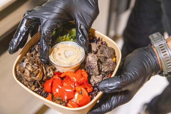 Restaurant chef assembling a fresh grain bowl with roasted vegetables, protein, and house-made dressing for healthy dining.