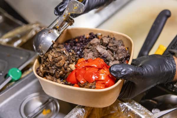 Fresh grain bowl being prepared with roasted vegetables, wholesome grains, and house-made toppings in a restaurant kitchen.